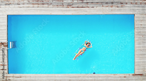 Outdoor lifestyle portrait of young pretty sexy girl floating with neon bright swimming mattress by the pool © skymediapro