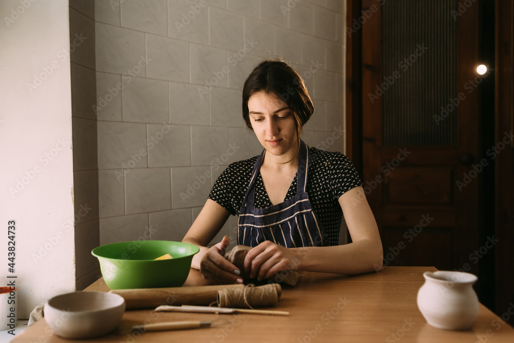 Focused woman working with wet clay in pottery. The beginning of the creation of the sculpture. Sitting at the table takes a piece of clay and tears it apart.
