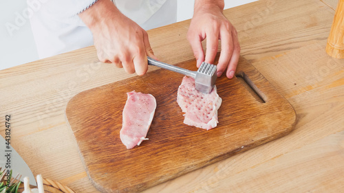 Cropped view of chef with chopping hammer flattening pork on table