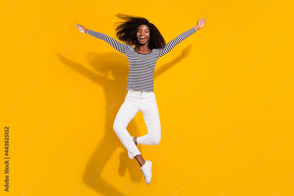 Full length body size photo woman jumping up laughing careless in striped shirt isolated vibrant yellow color background