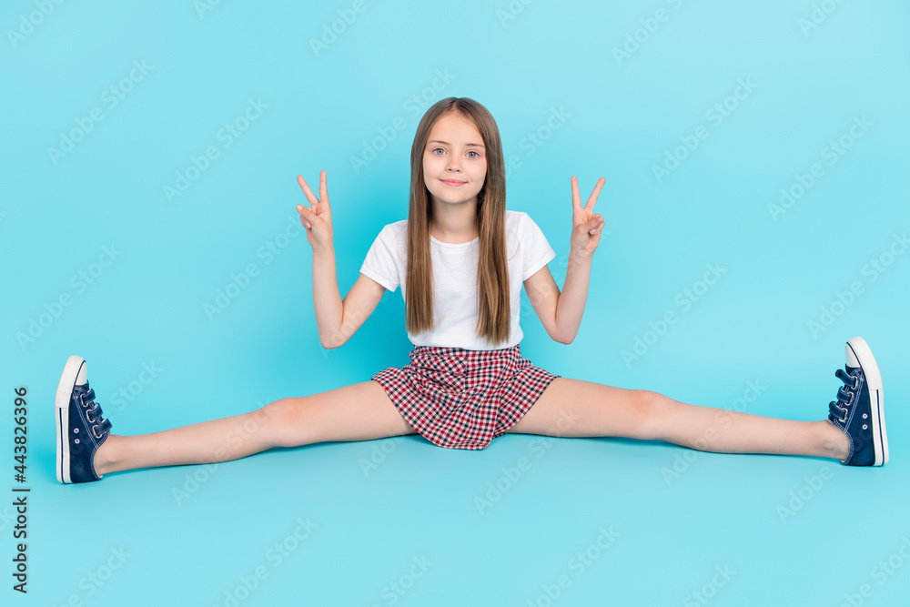Foto de Full size photo of cool brown hair small girl stretch show v-sign  wear white t-shirt skirt isolated on blue color background do Stock
