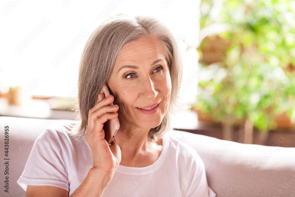 Photo of pretty charming lady pensioner wear white t-shirt sitting sofa smiling talking modern gadget waving arm indoors house flat Photo of pretty charming lady pensioner wear white t-shirt sitting sofa smiling talking modern gadget waving arm indoors house flat