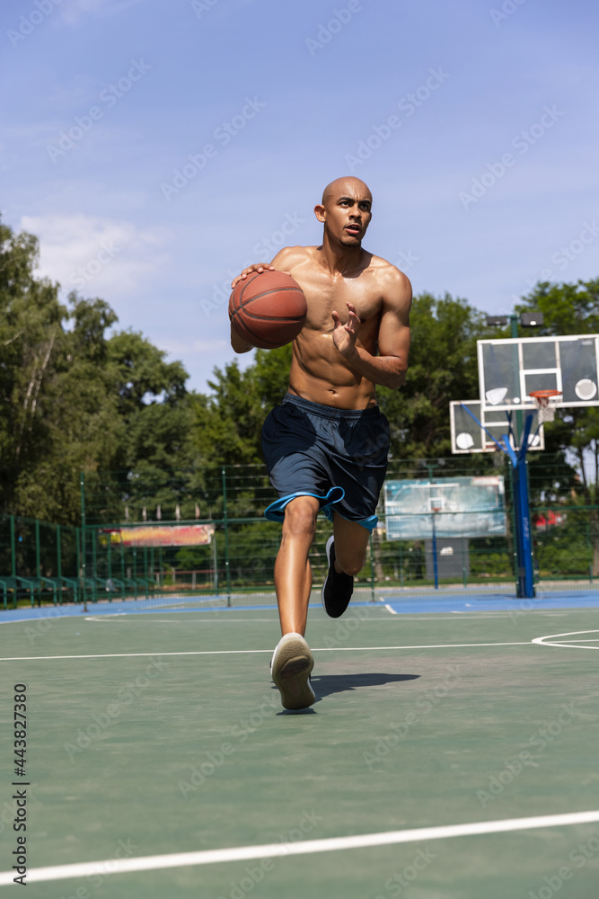 Young african-american male basketball player training at street public stadium, sport court or palyground outdoors. Summer sport games.