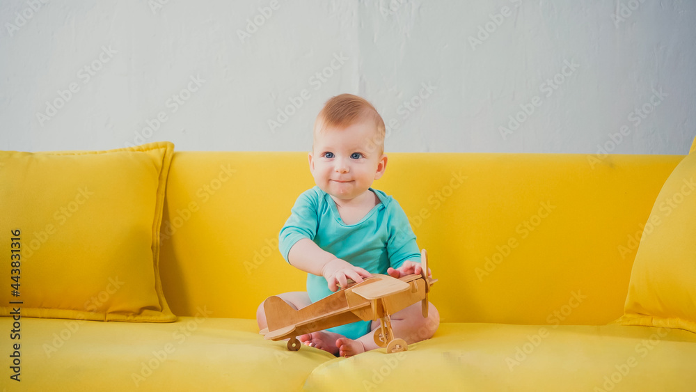 happy infant boy sitting on sofa and playing with wooden biplane happy infant boy sitting on sofa and playing with wooden biplane
