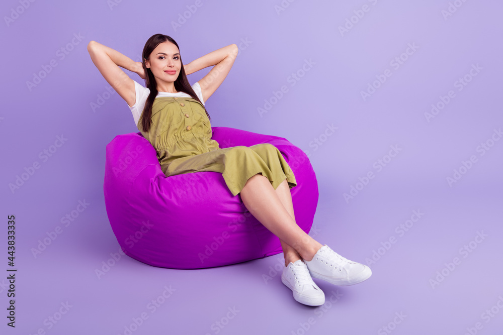 Full length photo of charming young happy woman relax hands behind head sit chair isolated on violet color background