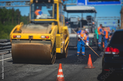 Process of asphalting and paving, asphalt paver machine and steam road roller during road construction and repairing works, workers working on the new road construction site, placing a layer in summer