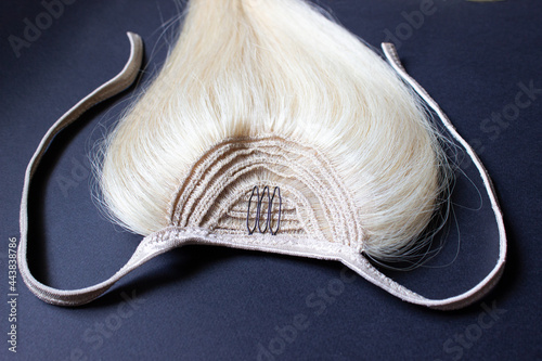 Blonde natural hair for extensions up close-up on a black background. A ponytail made of hair with dark corners and light ties.