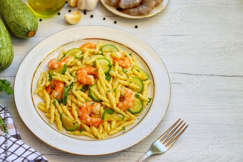 Italian Traditional Dish"Trofie con Gamberi e Zucchine",trofie pasta with prawns,zucchini,olive oil,garlics,parsley,salt and peppers on plate with white wood table background.Top view.Copy space