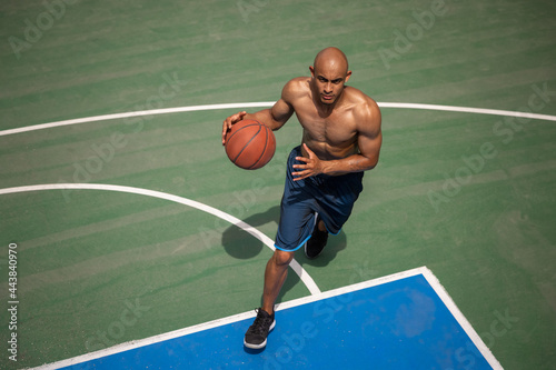 Strong muscular african-american male basketball player training at street public stadium, sport court or palyground outdoors. Concept of healthy active lifestyle, motion, hobby. photo