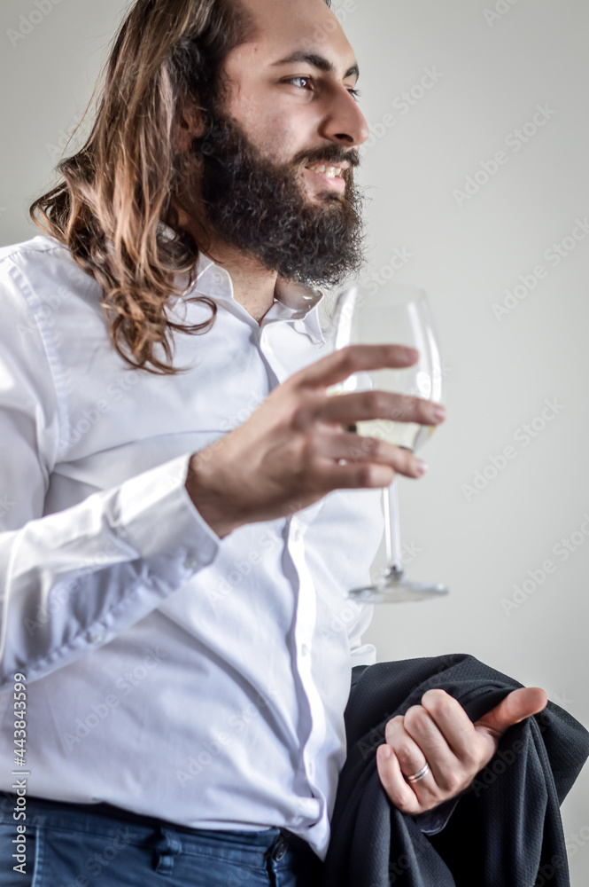 Portrait of a young middle eastern businessman with beard and long hair holding a glass of white wine and his jacket on his arm Portrait of a young middle eastern businessman with beard and long hair holding a glass of white wine and his jacket on his arm