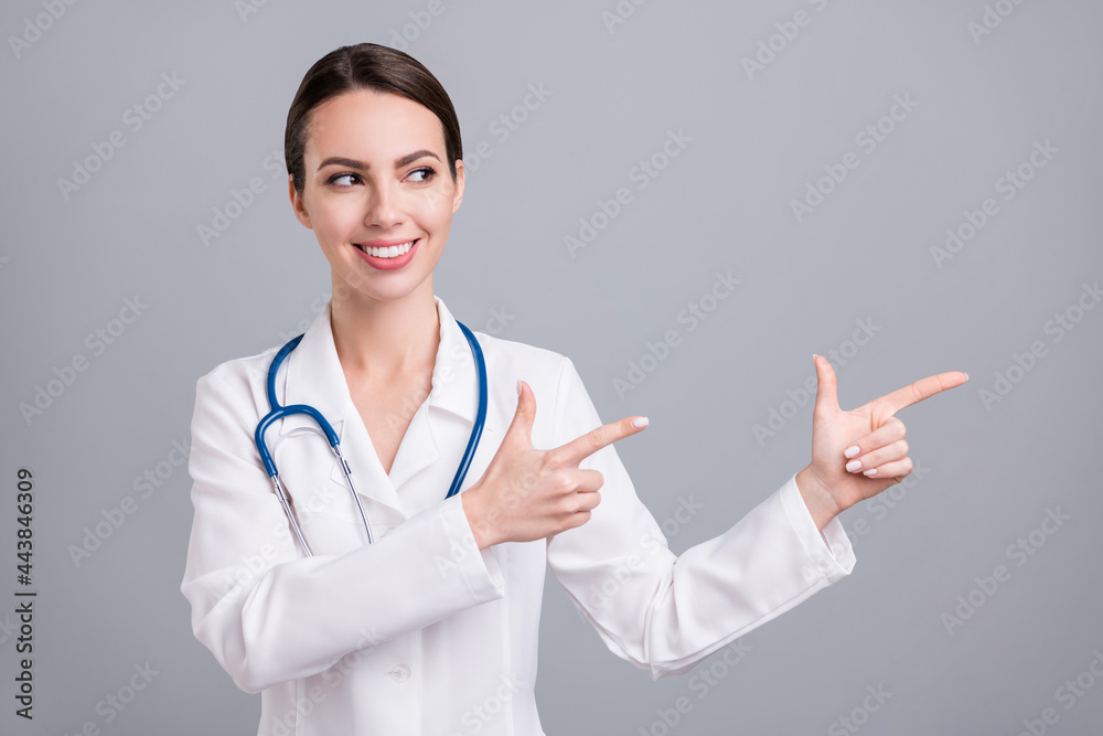 Photo of pretty charming young lady doctor workwear looking pointing fingers empty space smiling isolated grey color background Photo of pretty charming young lady doctor workwear looking pointing fingers empty space smiling isolated grey color background