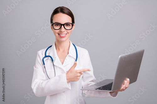 Photo portrait young nurse with sthethoscope smiling showing finger laptop isolated grey color background photo
