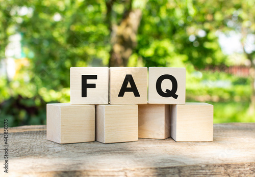 Three wooden cubes are stacked in the FAQ word. They lie on other cubes against the backdrop of the summer garden.