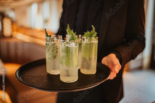 A close up shot of four refreshing cocktails on a black tray. Bartender holding the tray with cocktails. Concept of hospitality and leisure