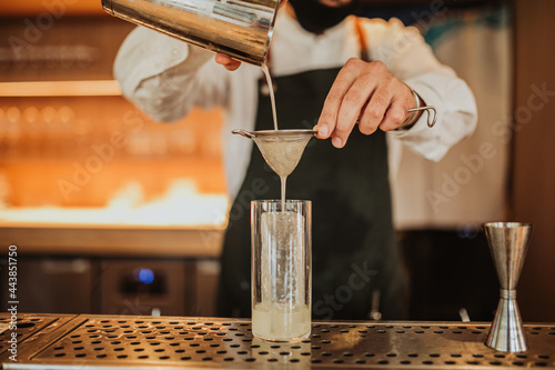 Close up shot of a bartender in a green apron making a cocktail. Concept of hospitality, leisure, restaurant and mixology. Focus on hands and a glass photo