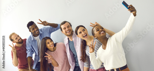 Happy cheerful laughing young adult diverse college student friends doing V sign hand gesture taking group phone selfie picture in studio, enjoying best time of life, making memories together. Header