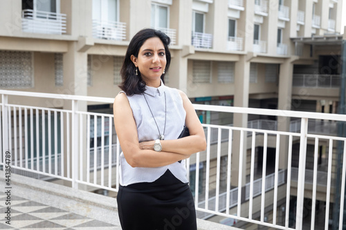 An Indian woman standing with her arms crossed in an urban corporate setting. Free Download An Indian woman standing with her arms crossed in an urban corporate setting. - GFXLoad