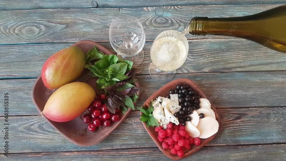 Two earthenware bowls - one with mango, cherries, basil and mint, the other with black currant, blue cheese, mozzarella and raspberries. Two glasses filled with dry white wine. Wood background