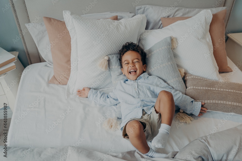 Portrait of afro american joyful little boy on pillows in bed laughing and smiling Portrait of afro american joyful little boy on pillows in bed laughing and smiling
