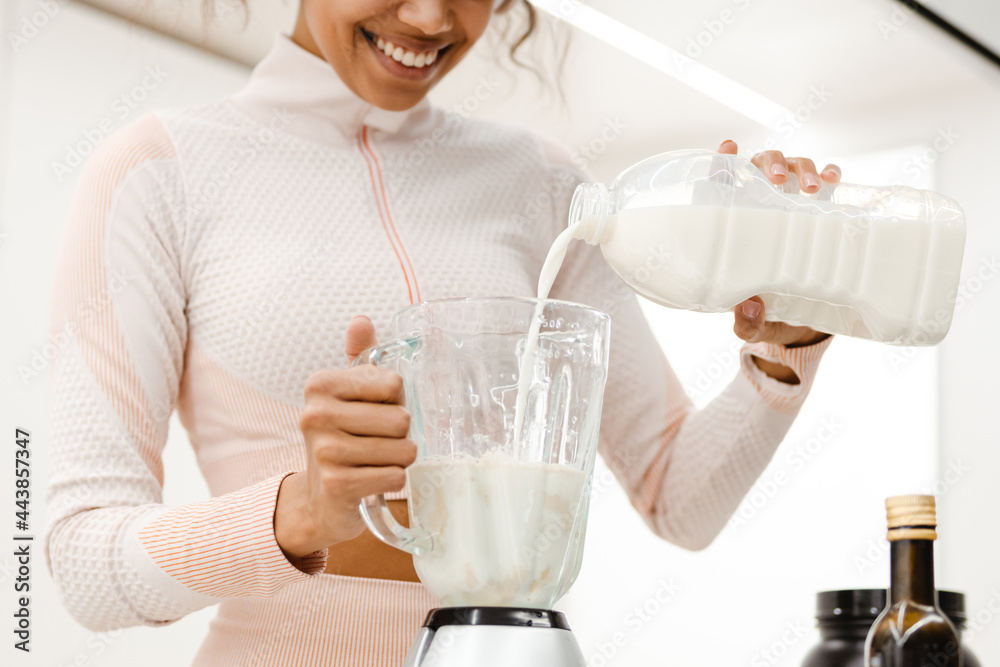 Black young woman smiling and making smoothie with milk Black young woman smiling and making smoothie with milk