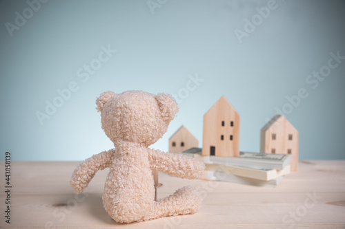 Concept loan, banking, and save money. Little brown teddy bears lookingat wood house models, and banknote stacks on an old wooden table with copy space. Savings money to buy a home for the future. photo