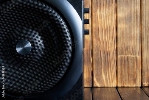 A large loud subwoofer in a wooden case with a metal grille and volume and tone controls stands against a background of natural planks. Audiophile concept. Scandinavian style. photo