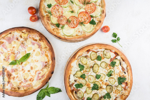 Three pizzas with different fillings of chicken, ham, mushrooms, pineapple, tomatoes, Mozzarella cheese and parmesan on a light background.