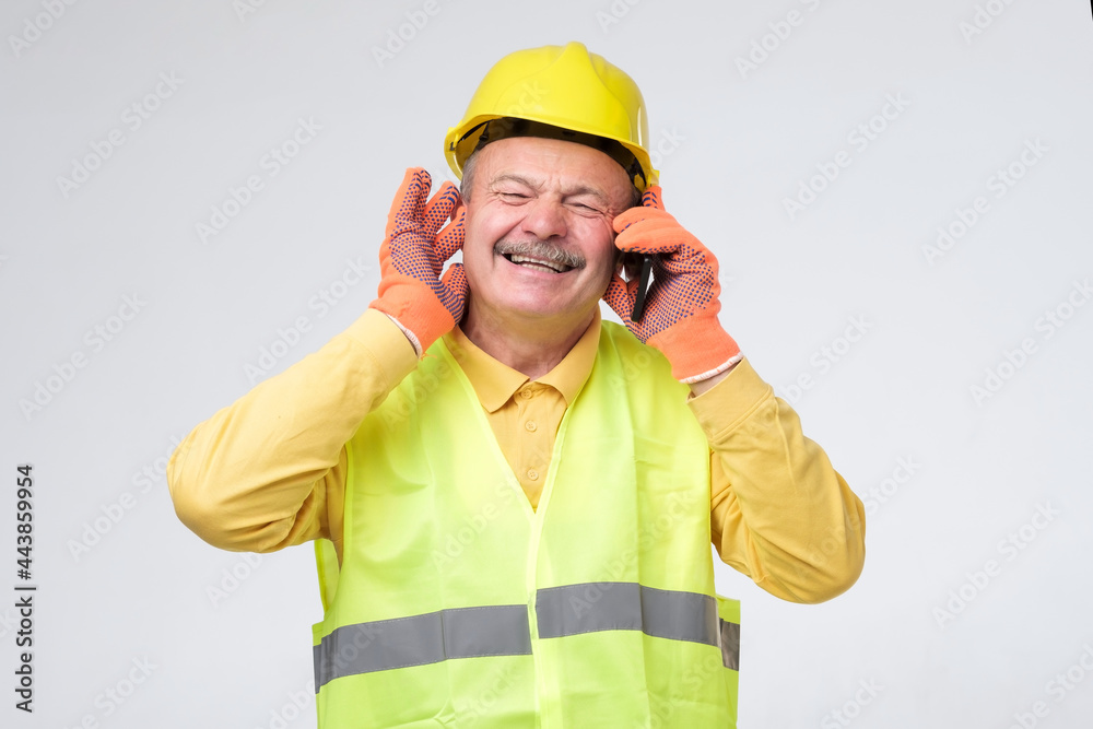 Worker wearing safety helmets close his other ears while talking on mobile phone