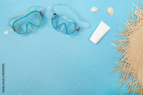 Top view photo of sunscreen diving masks, seashells, hat from above on isolated blue background with copyspace. Flat lay