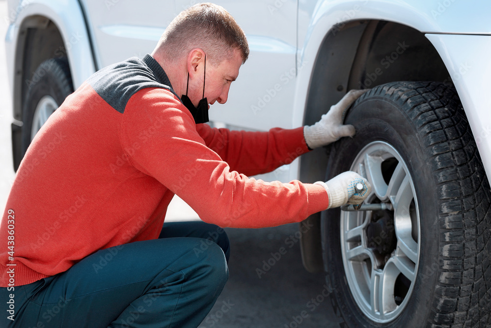 A man changes a wheel on a car on the street on a sunny day. Help on the road with a tire puncture. A man changes a wheel on a car on the street on a sunny day. Help on the road with a tire puncture.