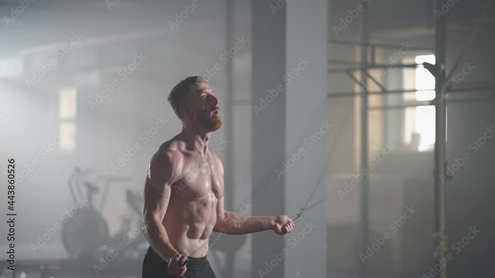 A young athletic man with prominent muscles jumps on a rope in the gym in slow motion