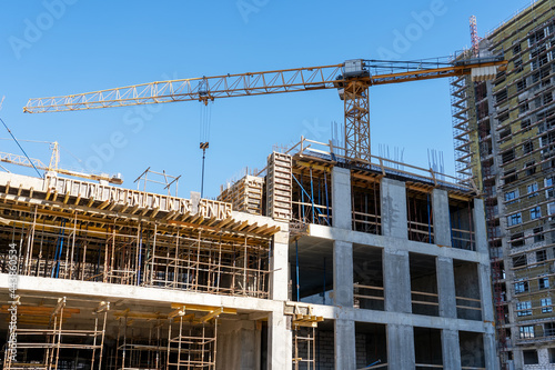 Construction cranes and unfinished residential buildings against clear blue sky. Housing construction, apartment block with scaffolding