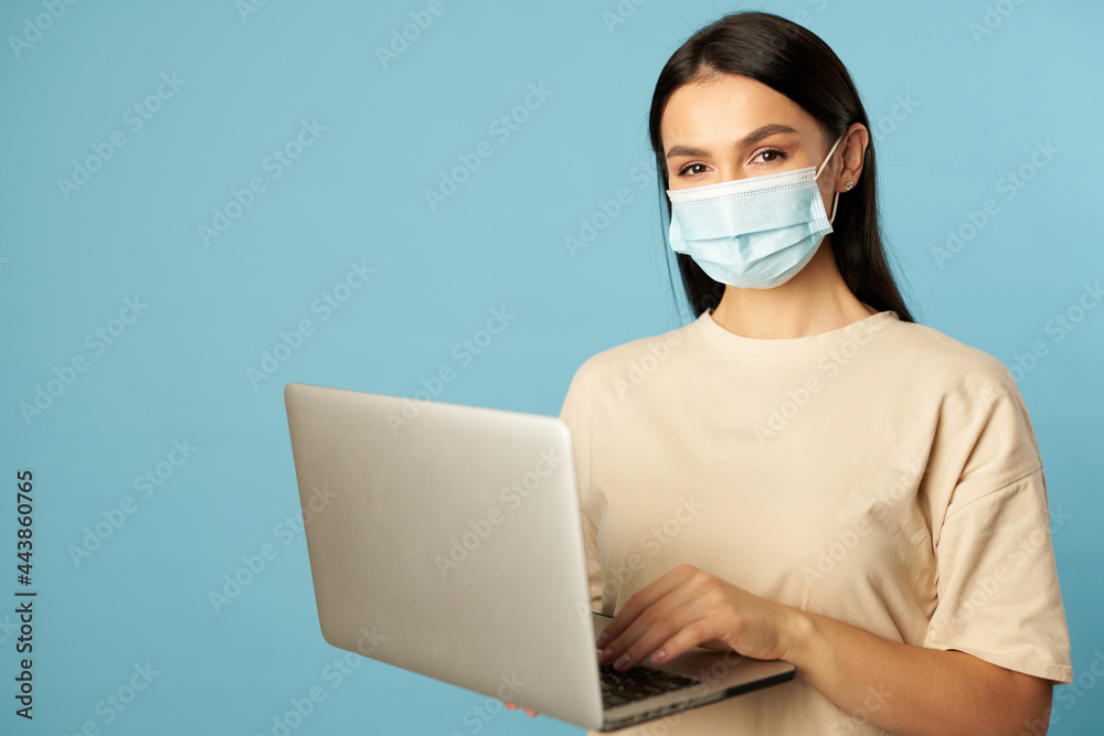 Pretty lady in face mask posing with laptop while typing Pretty lady in face mask posing with laptop while typing