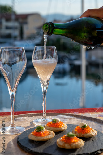 Russian style party with two glasses of white cold champagne, bliny with red caviar and view on Port Grimaud near Saint-Tropez in summer