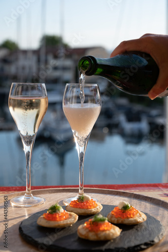 Russian style party with two glasses of white cold champagne, bliny with red caviar and view on Port Grimaud near Saint-Tropez in summer