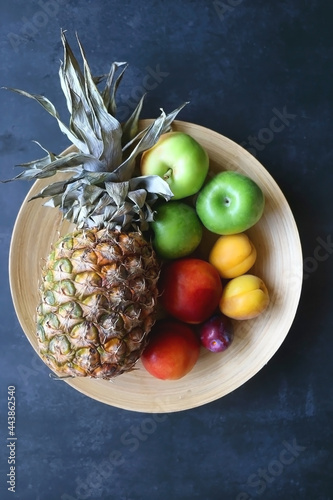 Wooden bowl with various colorful fruit on dark background. Top view.