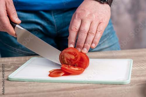 A man cuts a red tomato on a board. Healthy eating