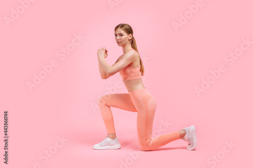 Fitness woman doing lunges exercises to train leg muscles, woman doing lunge exercise on one leg forward, on pink background