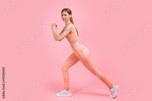 attractive athletic woman in pink tracksuit doing gymnastics and stretching legs isolated on pink background