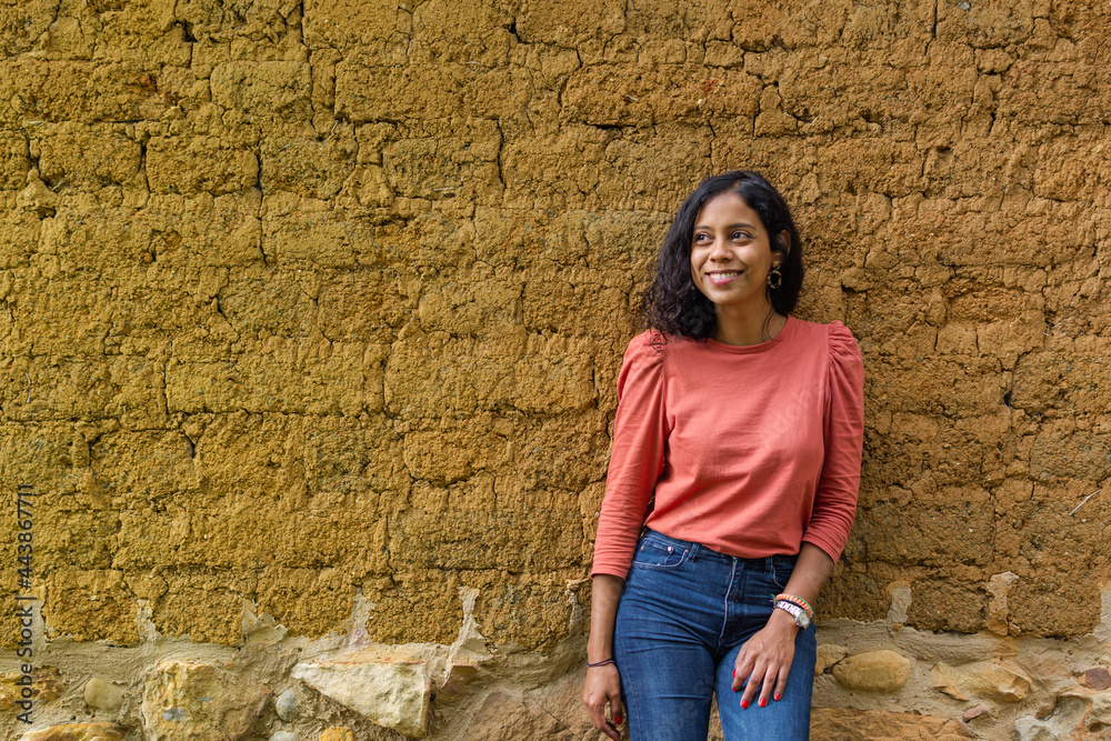 Medium shot of a beautiful Latina woman looking to the side and posing in a relaxed manner with an adobe wall in the background Medium shot of a beautiful Latina woman looking to the side and posing in a relaxed manner with an adobe wall in the background