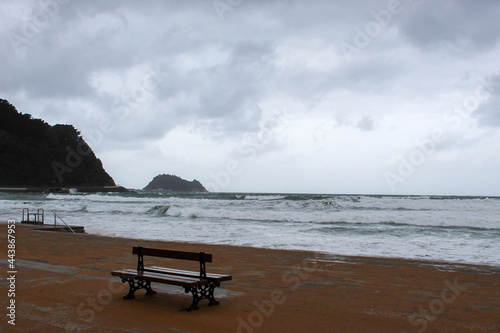 a lonely bench in the sea with waves and a cloudy winter sky