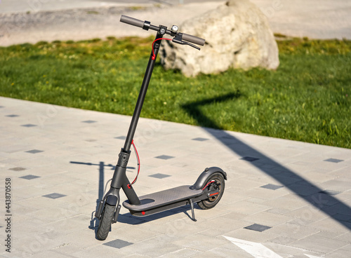 Electric scooter parked on tiled stone pavement green lawn background