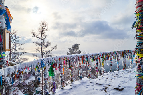 Buddhist multicolored wish ribbons at a height in the mountains above Lake Baikal in Russia. High landscape with Fencing with colored ribbons on a cliff with trees