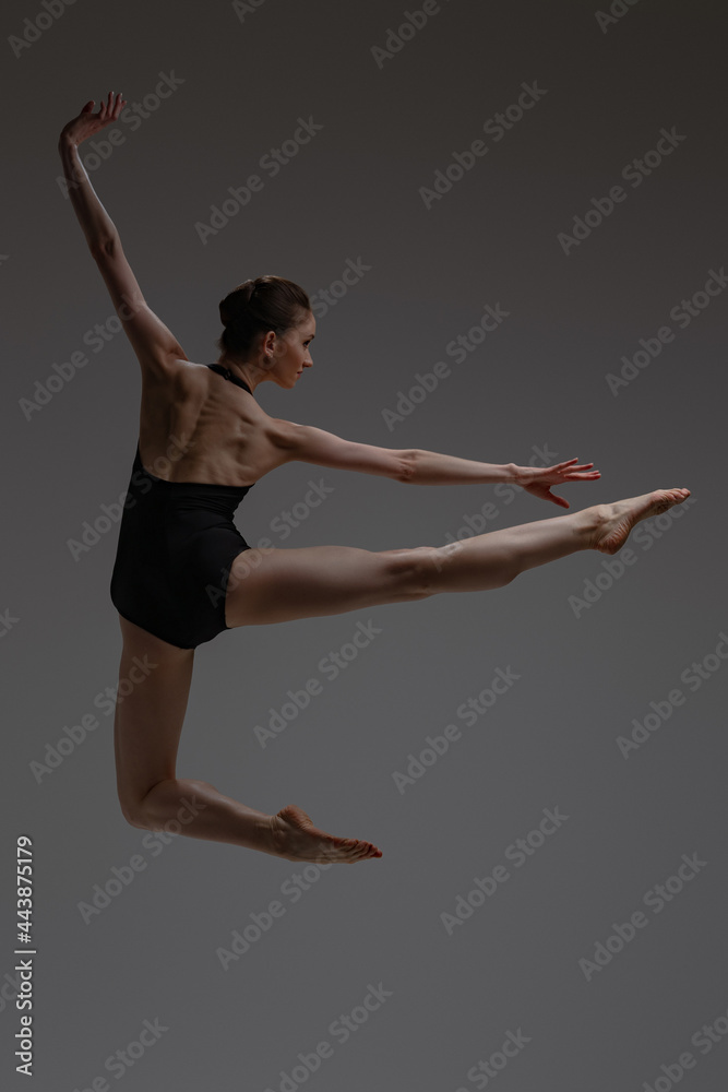 Fototapeta premium Sideview shot of jumping ballerina against gray background