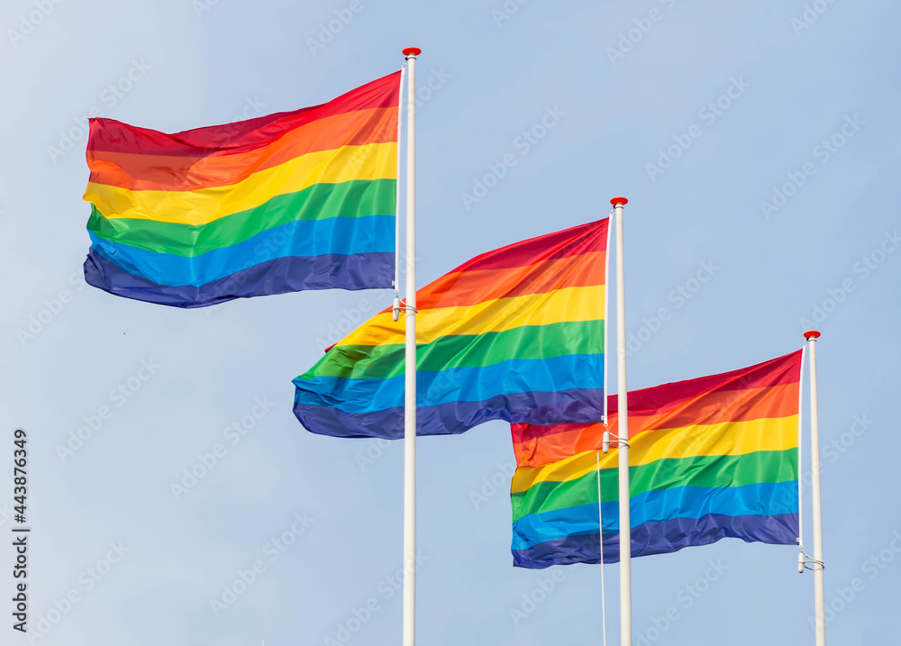 Three colorful rainbow flags, a symbol of LGBT, gay pride symbol on the blue sky background. Three colorful rainbow flags, a symbol of LGBT, gay pride symbol on the blue sky background.