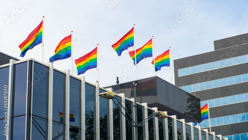Obraz na płótnie A rainbow gay flags, symbols of LGBT+ pride and equality symbol on the roof of a modern city building. w salonie