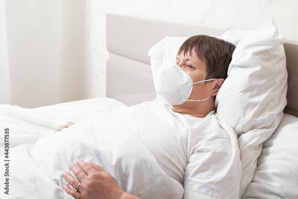 An infected elderly woman on the bed. Grandmother in a medical mask. An infected elderly woman on the bed. Grandmother in a medical mask.