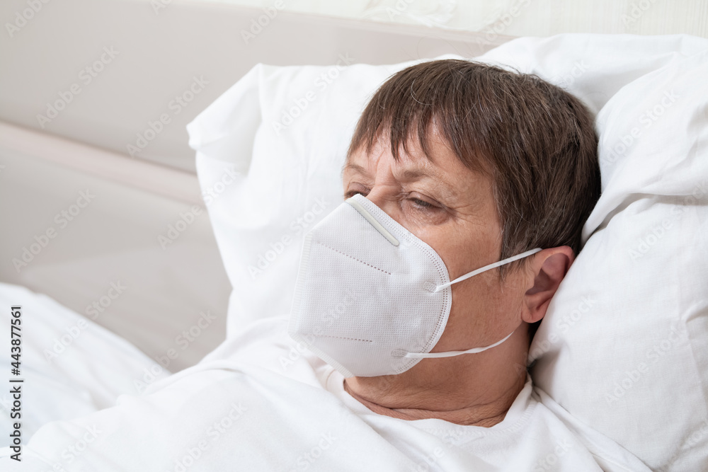An infected elderly woman on the bed. Grandmother in a medical mask. An infected elderly woman on the bed. Grandmother in a medical mask.