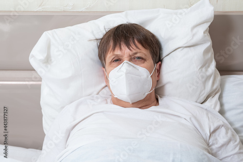 An infected elderly woman on the bed. Grandmother in a medical mask.