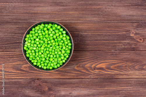 Fresh green peas in a bowl on a brown wooden table. View from above. Place for an inscription.
